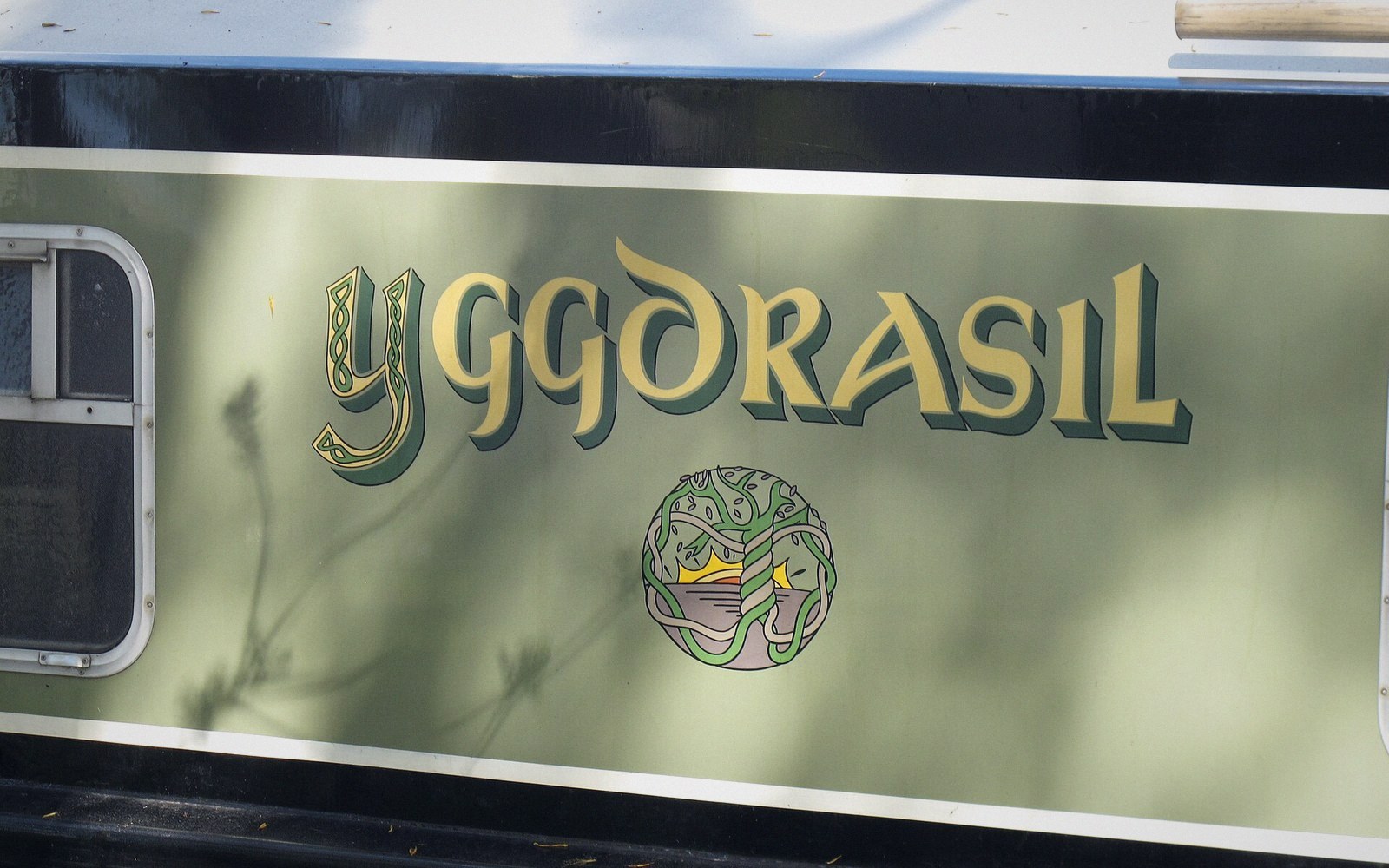 Painted "Yggdrasil" name and tree emblem on a canal boat's hull panel