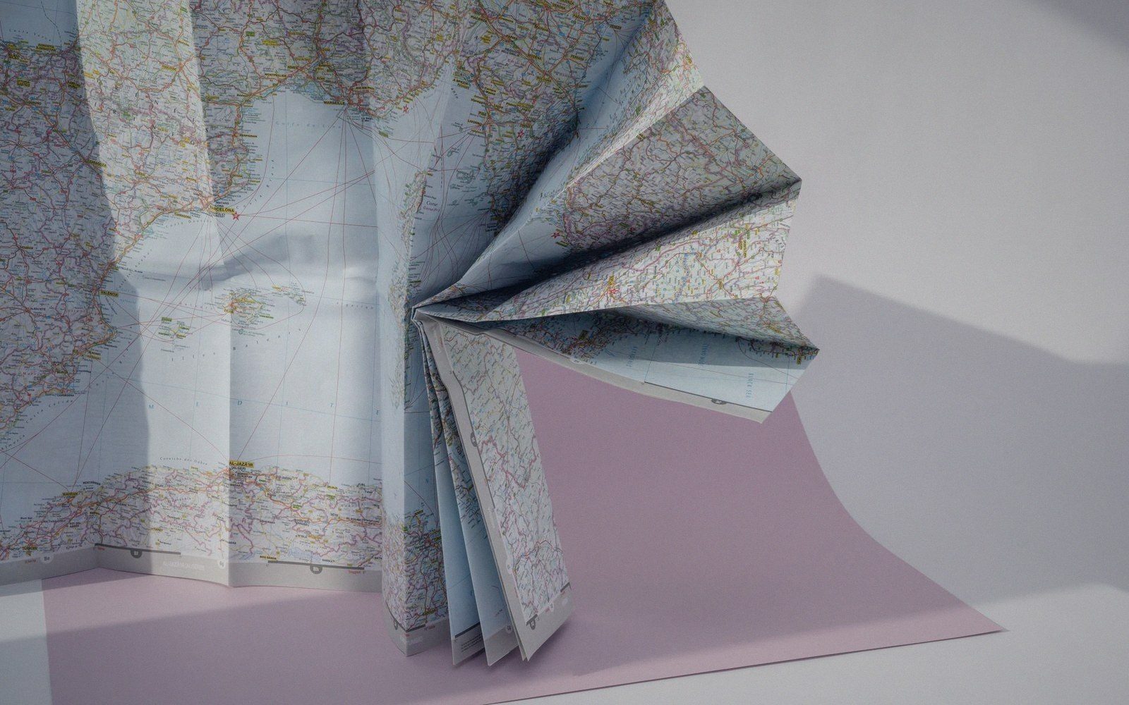A folded paper map accordion-pleated into a fan shape against a pink backdrop