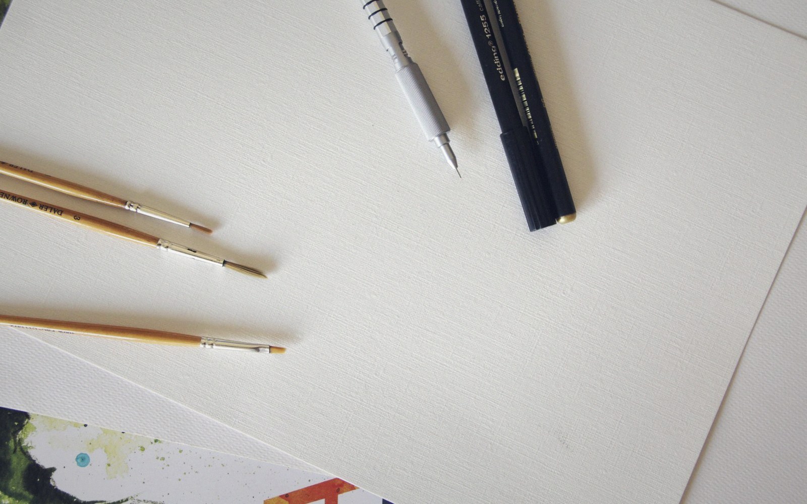 Paintbrushes, a mechanical pencil and a pen resting on blank textured paper