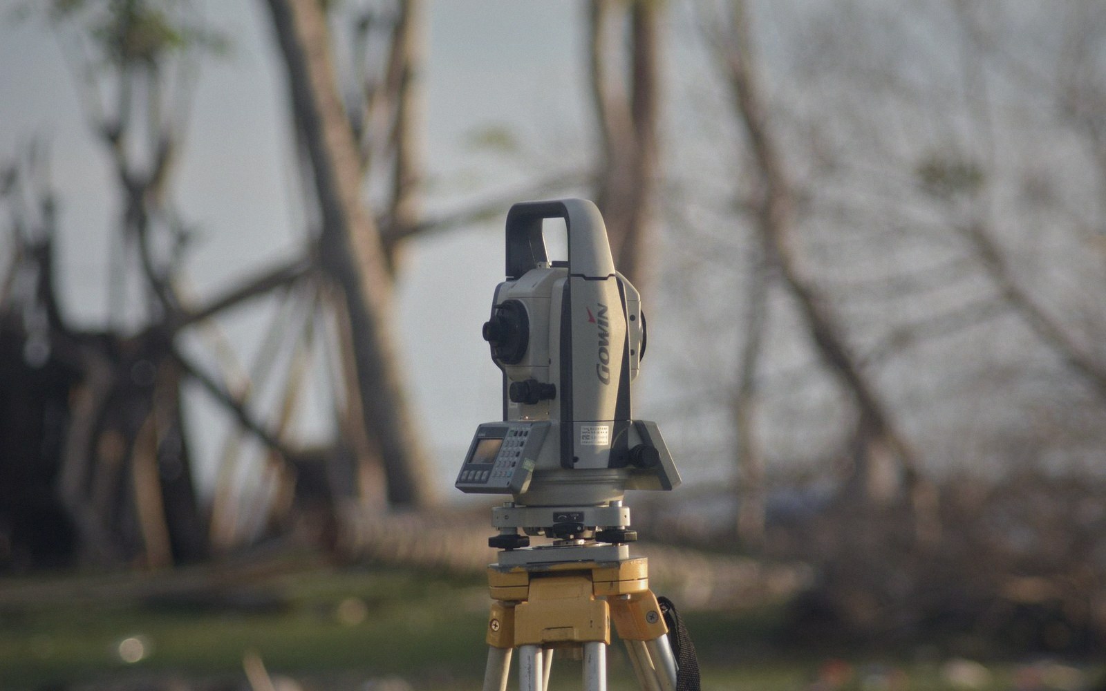 A surveyor at a tripod instrument in a field